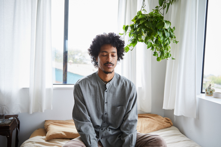Young man sitting on his bed and meditating with his eyes closed iStock 1270418885